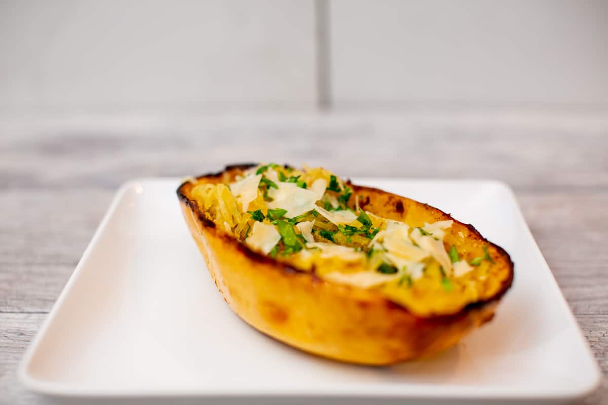 Spaghetti squash garnished with cheese and herbs on a square white plate placed on a white wooden table