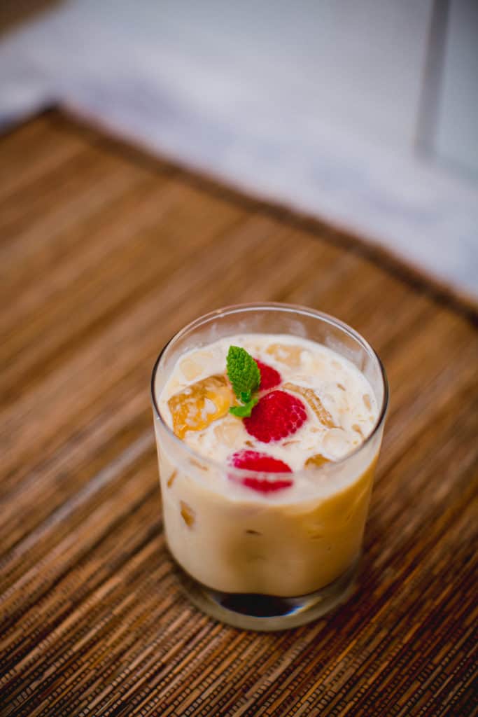 A glass of eggnog white Russian cocktail garnished with mint and raspberries