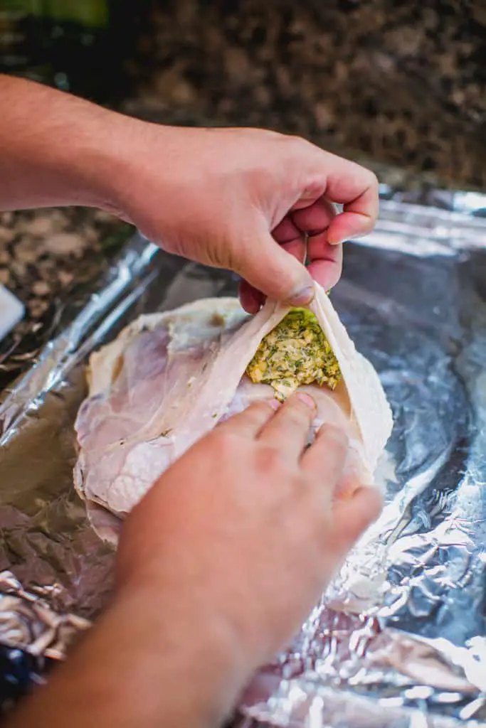 Person stuffing butter and herbs into a turkey breast