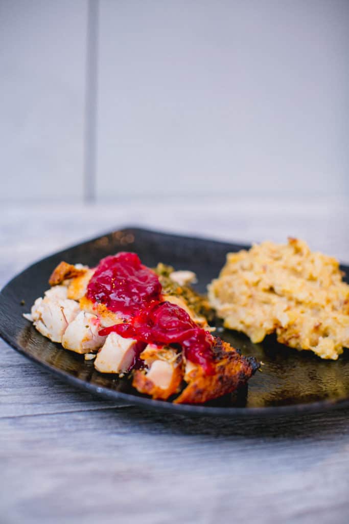 A plate of oven roasted turkey topped with cranberry sauce and paired with a side dish