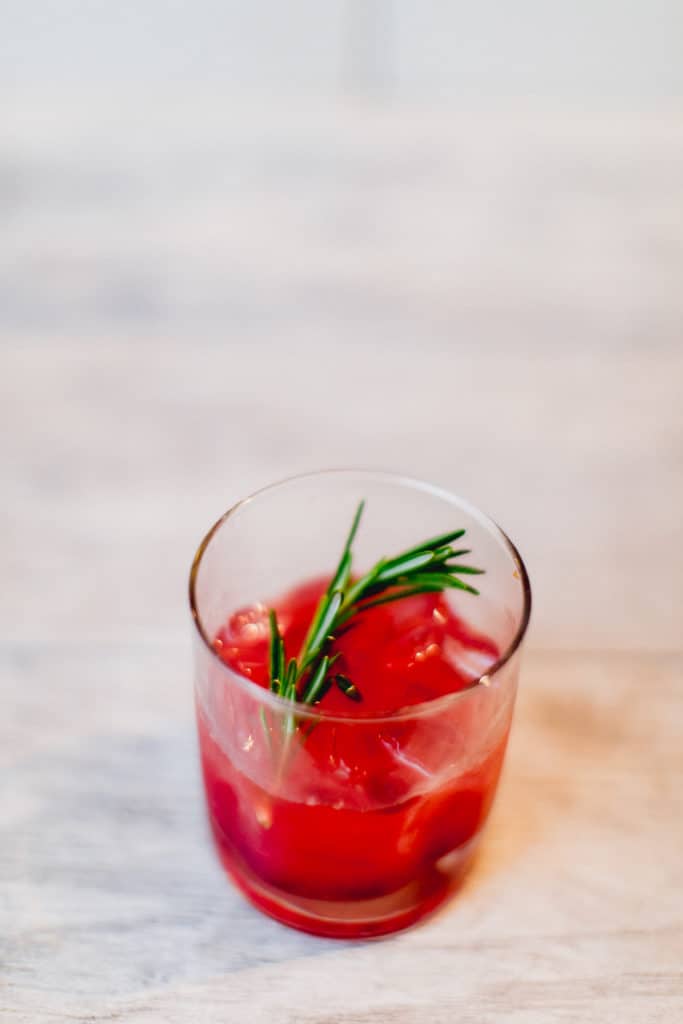 A cranberry bourbon smash cocktail with mint in a clear glass placed on a white surface