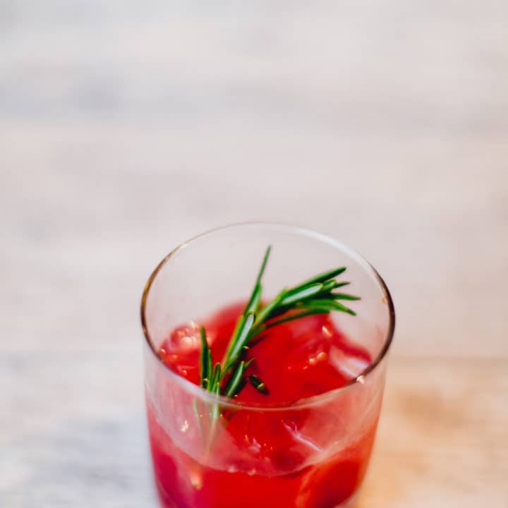 A cranberry bourbon smash cocktail with mint in a clear glass placed on a white surface