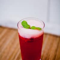 Cranberry champagne cocktail garnished with mint served in a clear glass put on a wooden placemat