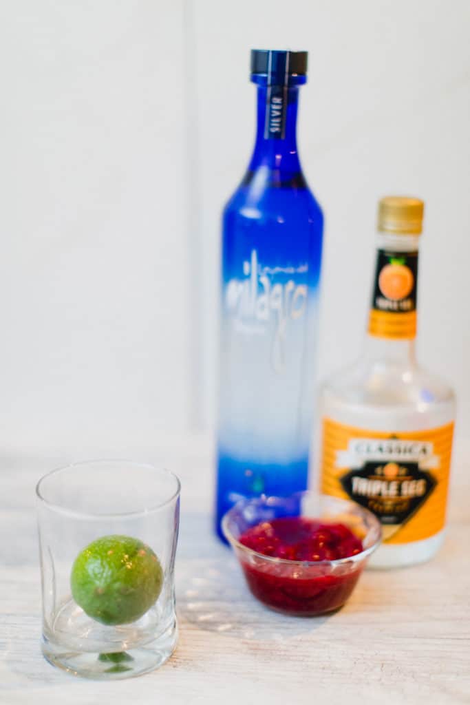 A lime, cranberries, tequila, and triple sec laid out on a table