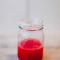 A cranberry margarita cocktail in a glass rimmed with salt placed on a white surface