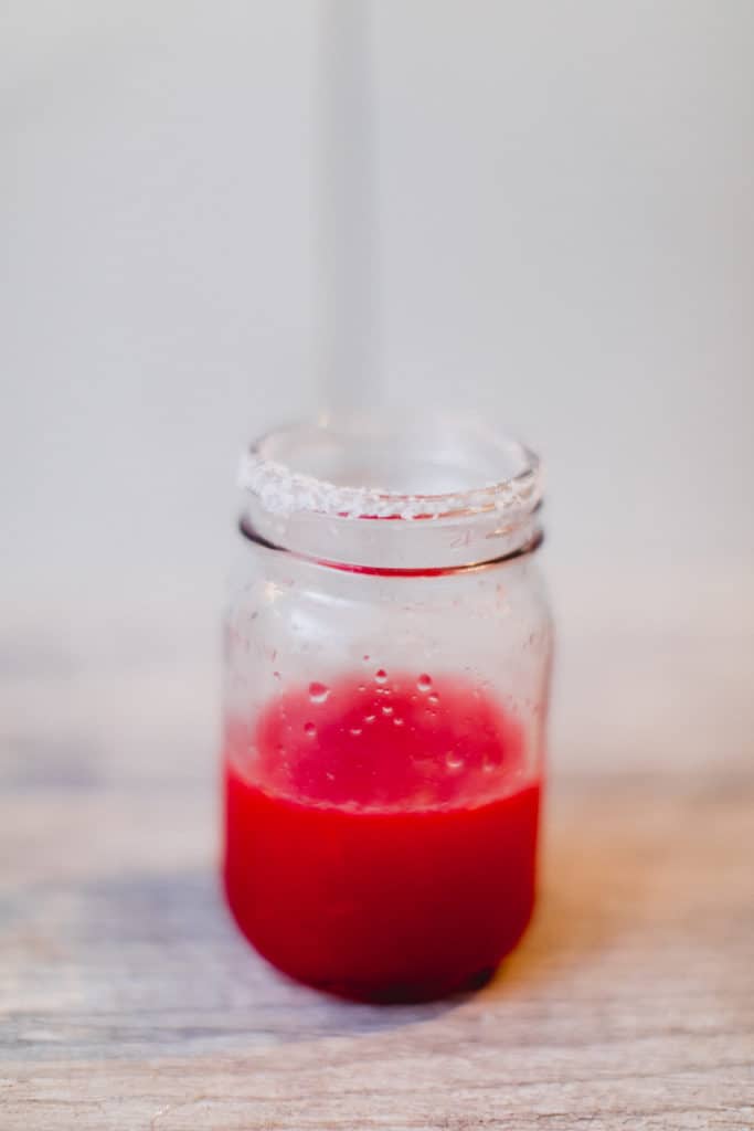 A cranberry margarita cocktail in a glass rimmed with salt placed on a white surface