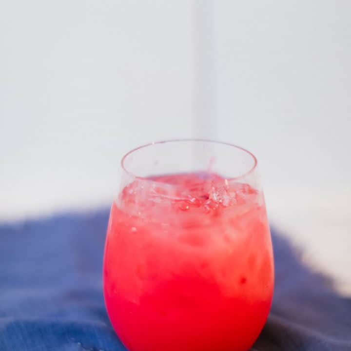 An ice-cold cranberry sea breeze cocktail served in a glass placed on a blue cloth