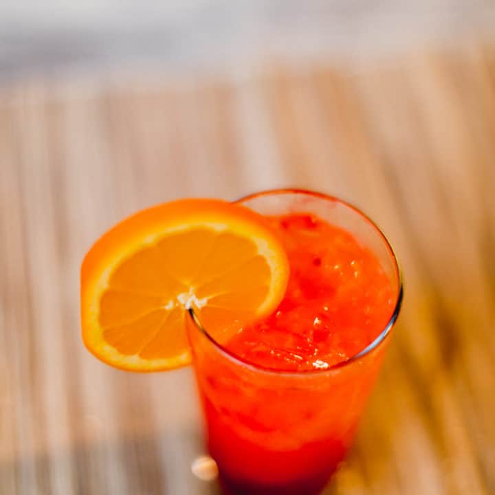 A top view of a tequila sunrise cocktail with a slice of orange in a glass placed on a brown surface
