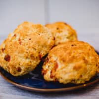 Three pieces of freshly baked cheesy biscuits are served on a blue plate placed on a wooden surface