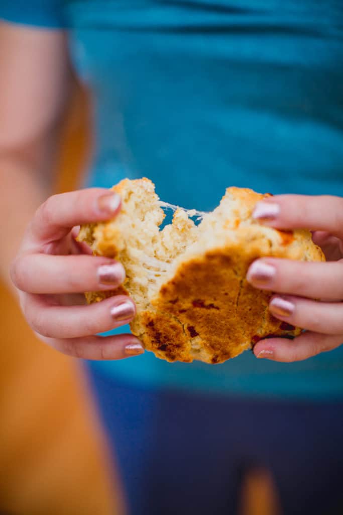 Person tearing apart a cheesy biscuit with strings of cheese visible