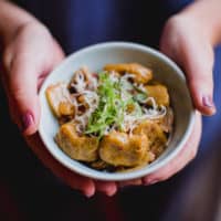 A person holding a bowl of butternut squash gnocchi garnished with parmesan cheese and herbs