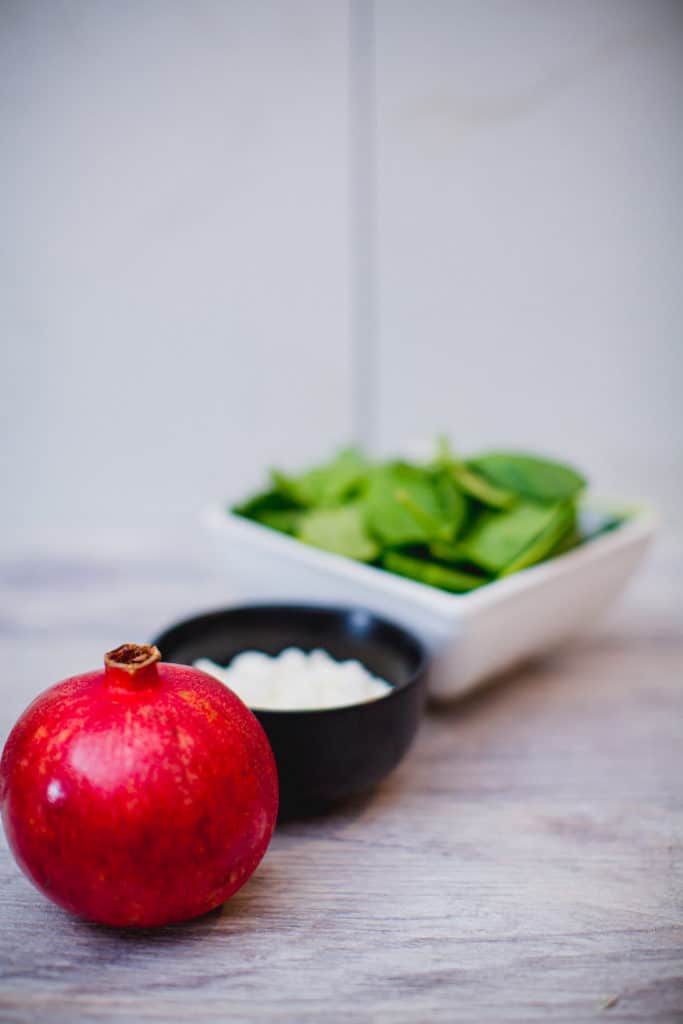 Pomegranate, arugula and a bowl of feta cheese in a table