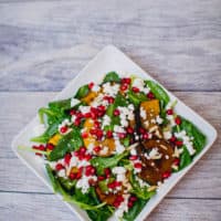 A top view of roasted acorn squash and pomegranate spinach salad served on a white plate put on a wooden surface