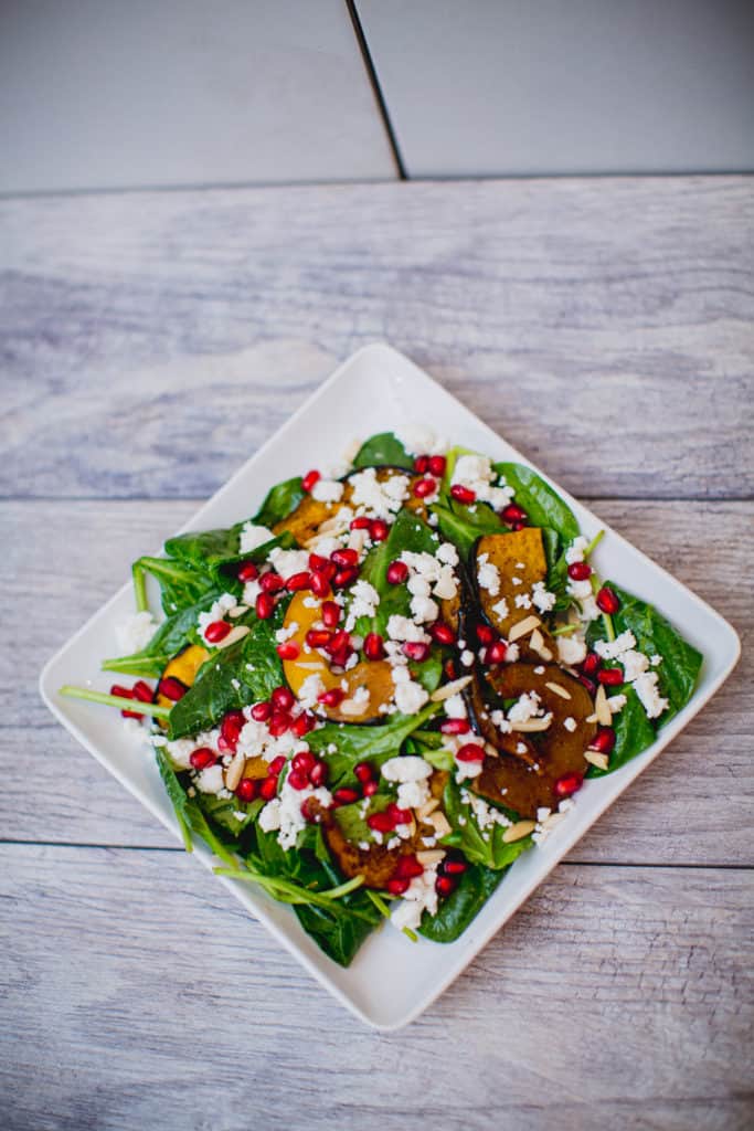 A top view of roasted acorn squash and pomegranate spinach salad served on a white plate put on a wooden surface