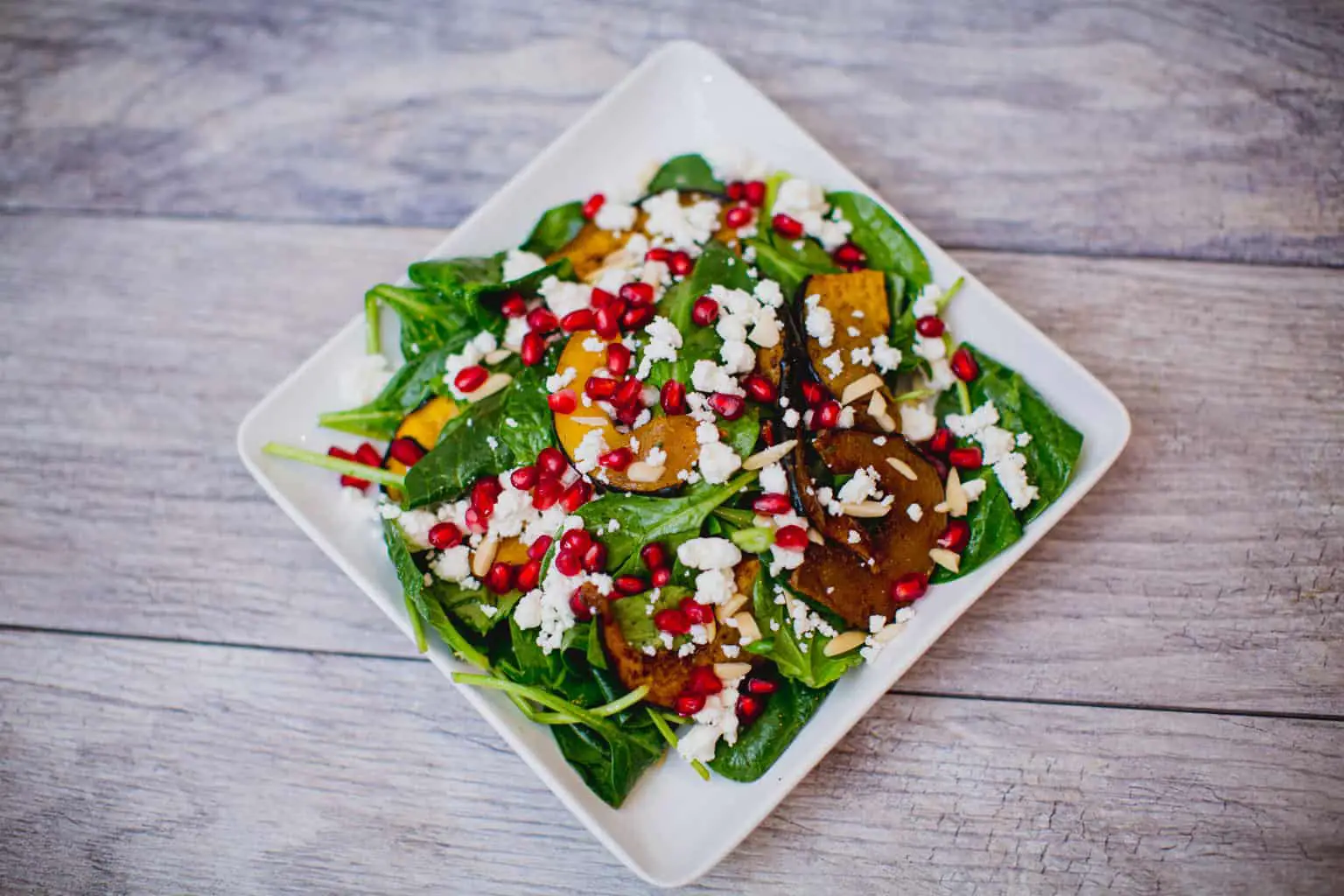 Roasted acorn squash and pomegranate spinach salad recipe in a white plate