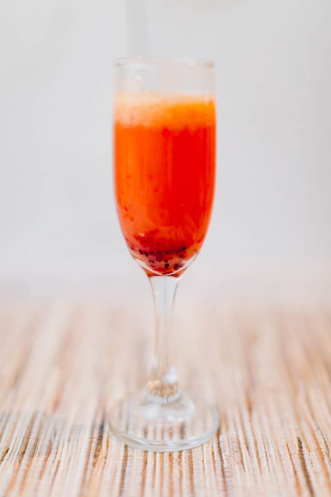 An orange cranberry mimosa served on a wine glass placed on a brown placemat