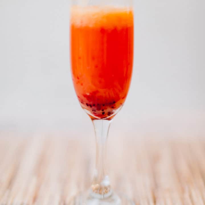 An orange cranberry mimosa served on a wine glass placed on a brown placemat