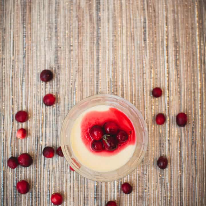 A top view of eggnog panna cotta with cranberry sauce near fresh cranberries placed on a placemat