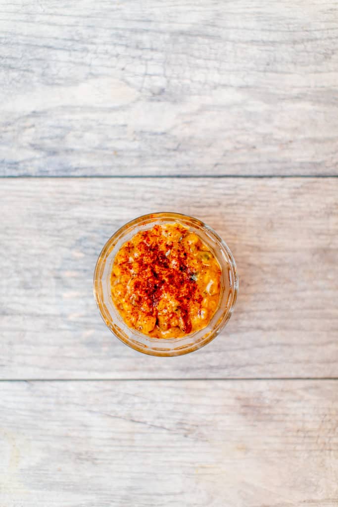 A top view of creamed corn is served in a small clear bowl placed on a wooden surface