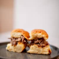 Two pieces of buns filled with Kalua pork are served on a black plate put on a wooden surface