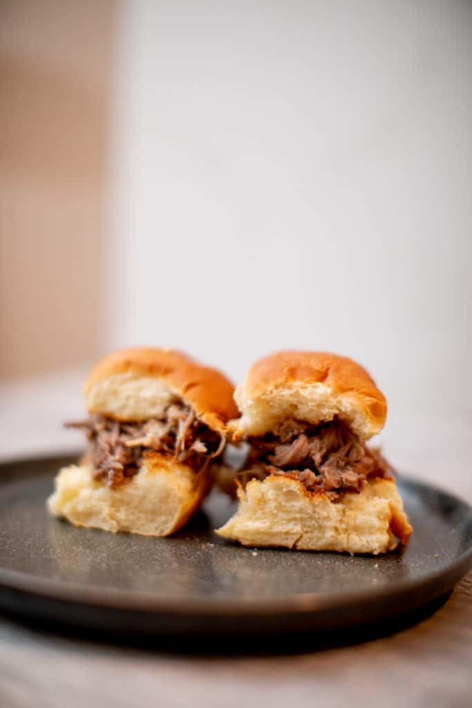 Two pieces of buns filled with Kalua pork are served on a black plate put on a wooden surface