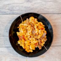 A top view of baked mac and cheese served in a black bowl placed on a wooden surface