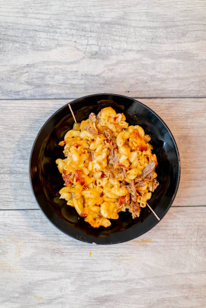 A top view of baked mac and cheese served in a black bowl placed on a wooden surface