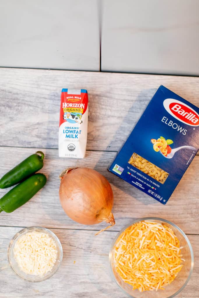 Milk, pepper, box of macaroni, onion, and two kinds of cheese in a bowl placed in a table