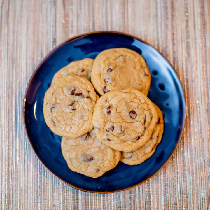 Chewy chocolate chip cookies on a ceramic blue plate placed on a brown placemat