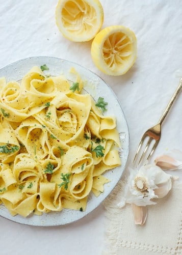 Prepared lemon and capers pasta sauce recipe on a plate with squeezed lemons and garlic on the side