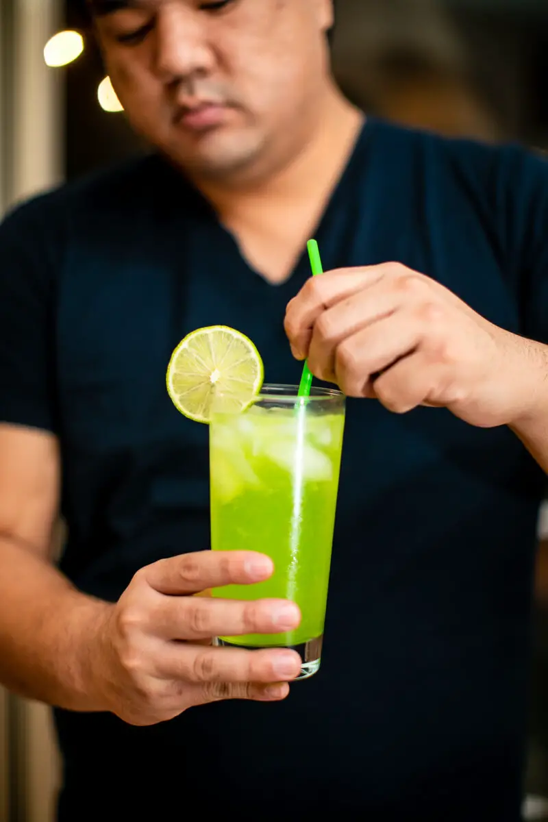 Man stirring a Lime White Claw cocktail with a straw in his hand