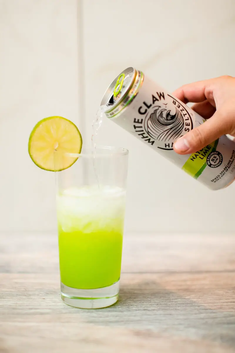 Man pouring a Lime White Claw into a glass with a Midori and vodka mix in it