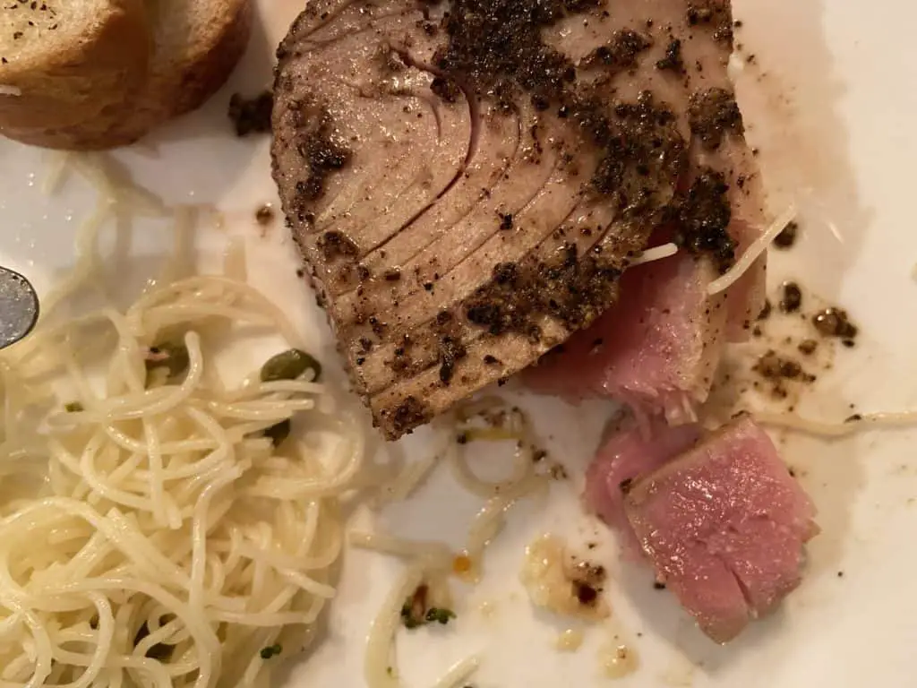 A top view of peppered seared ahi with pasta and bread served on a white plate