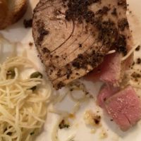 A top view of peppered seared ahi with pasta and bread served on a white plate