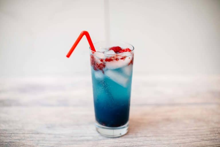 An ice-cold sour raspberry white claw cocktail with rum in a tall glass with a red bendy straw placed on a wooden table
