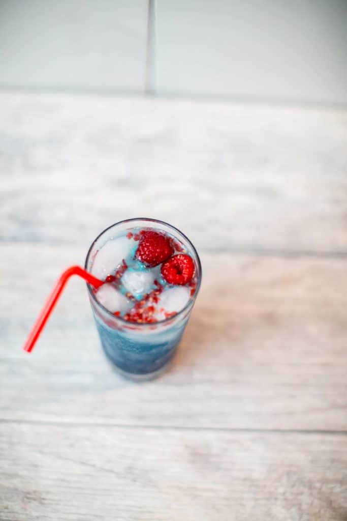 Close up of a raspberry white claw cocktail with rum in a tall glass with a red bendy straw