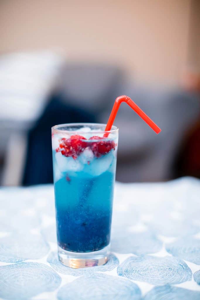 Sour raspberry white claw cocktail with rum in a tall glass with a red bendy straw placed on a table