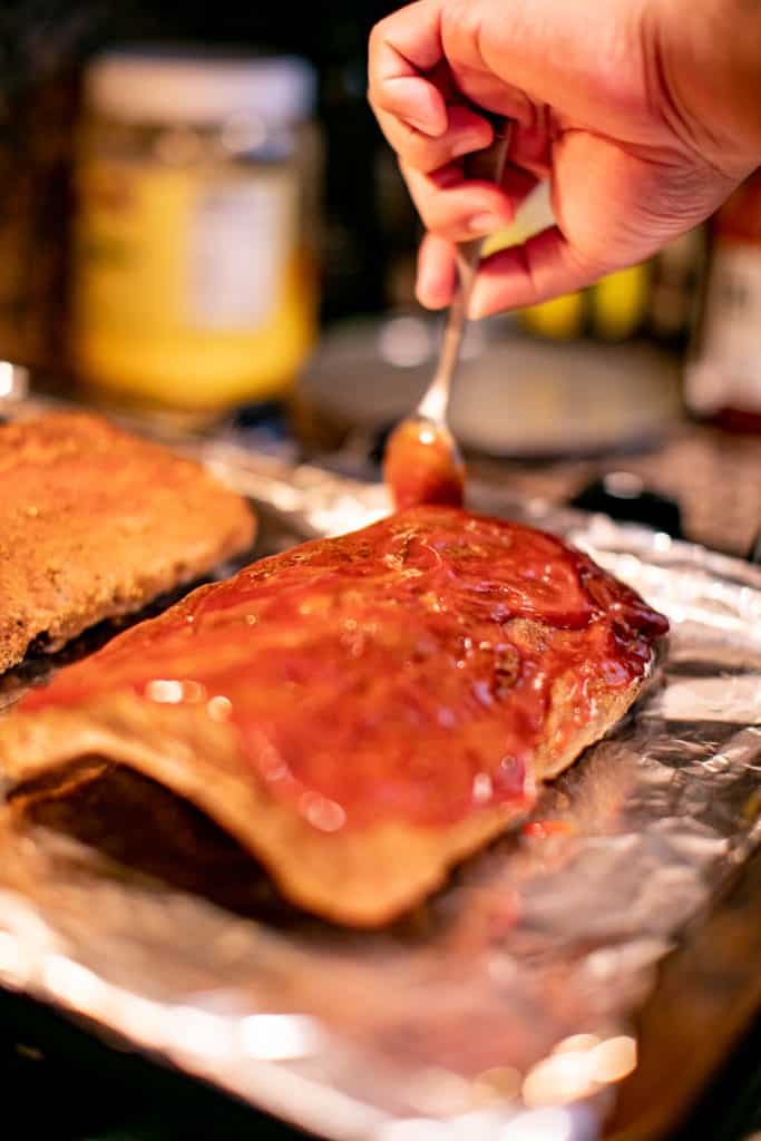 Person putting seasoning on a baby back rib through a spoon