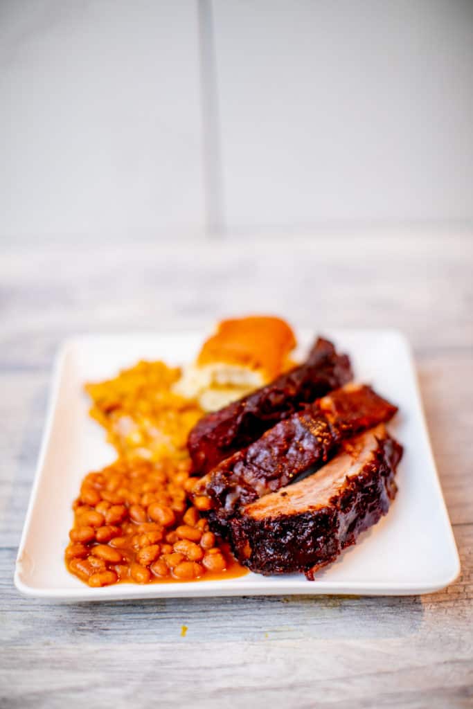 A sous vide baby back ribs with beans and dinner rolls on a plate