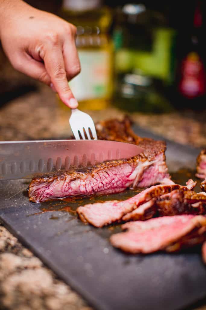 Person cutting a cooked steak with knife and fork