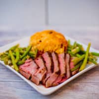 Sous vide bone-in ribeye with string beans and bread served on a square white plate placed on a wooden table