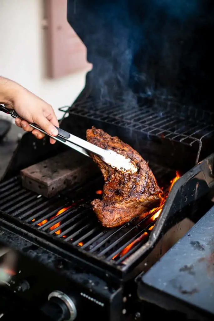 Person putting a seasoned tri tip on a grill