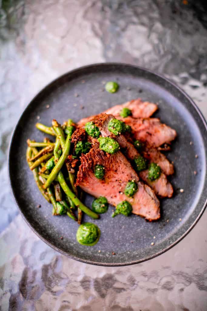 Sous vide tri tip meat with string beans served on a black plate placed on a glass table