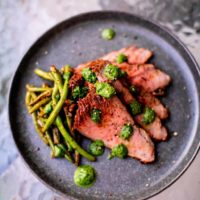 Sous vide tri tip meat with string beans served on a black plate placed on a glass table