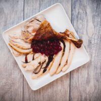 A top view of sliced dry brine turkey with sauce served on a square white plate placed on a wooden table