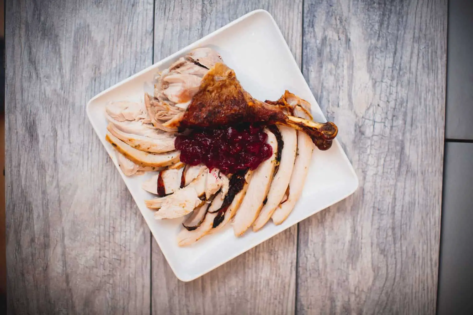 A top view of sliced dry brine turkey with sauce served on a square white plate placed on a wooden table