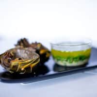 Roasted artichokes served on a black plate with lemon garlic butter sauce in a small glass bowl placed on a white table