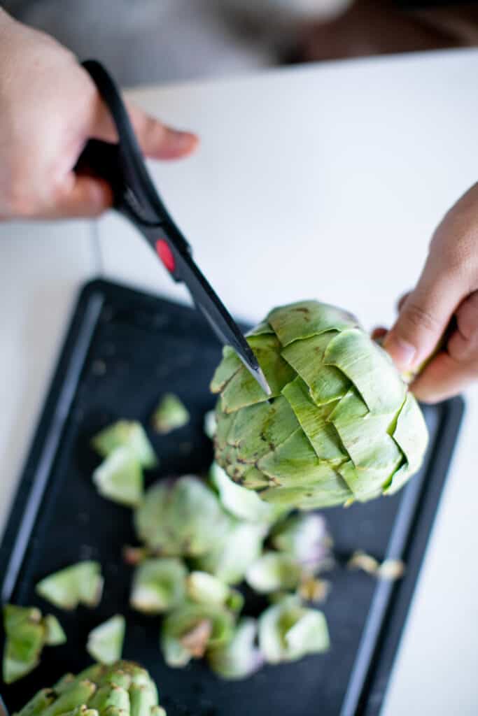 Person using kitchen shears to cut artichokes