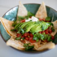 Cheese quesadilla garnished with tomatoes and avocado served in a ceramic green bowl placed on a white surface