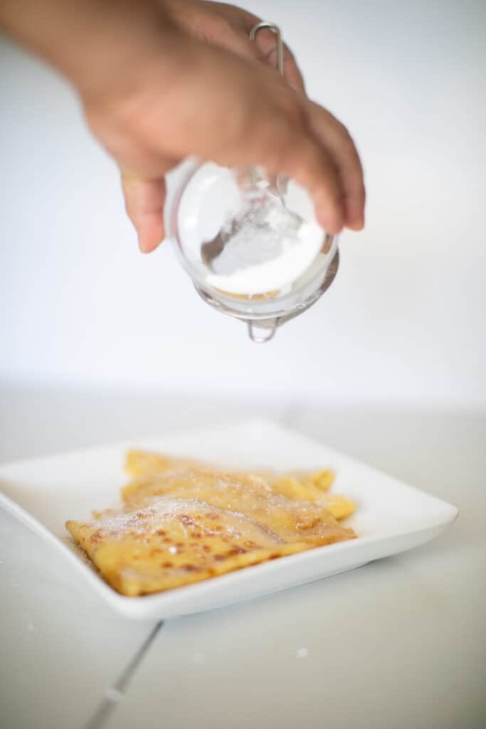 Dusting powdered sugar on top of a plate of crepe suzette